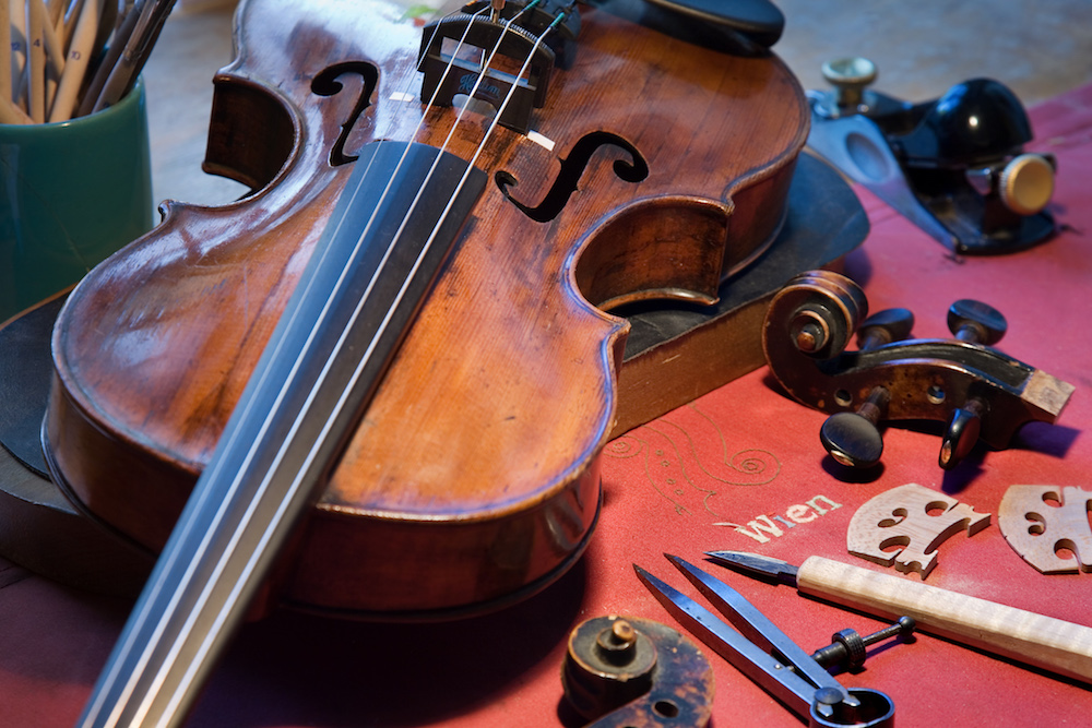 Geige auf einem mit Stoff ausgelegten Arbeitstisch mit Werkzeugen und Ersatzteilen
