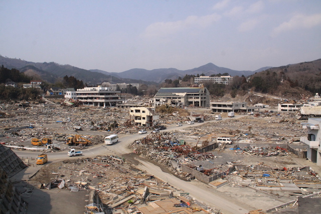 Onagawa in Trümmern, nur die Fassaden von einigen Gebäuden aus Stahlbeton stehen noch, im Hintergrund auf einem Hügel das Krankenhaus.