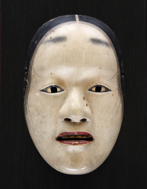 Nō-Maske vor schwarzem Hintergrund, Typ deigan, d.h. eine Frau mit golden untermalten Augen.