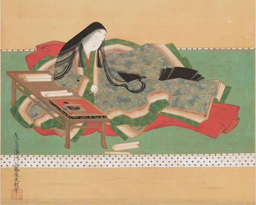 Murasaki Shikibu in der aufwendigen Kleidung der Hofdamen, auf einen niedrigen Schreibpult aufgestützt, einen Pinsel in der Hand. Auf dem Pult und dem Boden Schriftrollen verteilt.