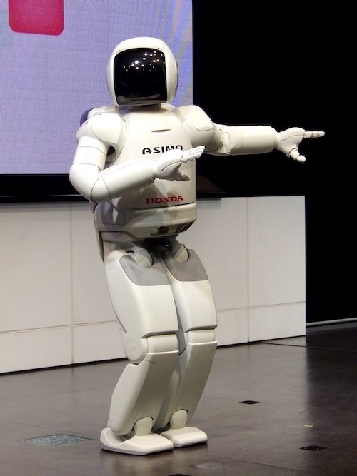 Weißer, menschenähnlicher Roboter, bei dem das Gleichgewicht sehr gut austariert ist, der Roboter streckt beim Tanzen die Arme zur Seite.