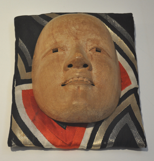 fertig geschnitzte Nō-Maske, abgelegt auf einem wertvollen Kissen, noch unbemalt