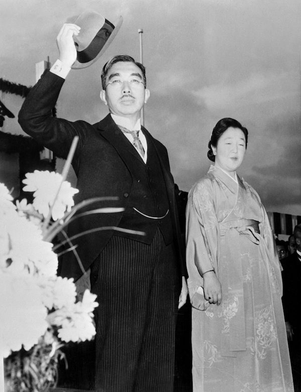 Schwarzweiß-Foto von unten: Tennō Hirohito grüßt mit seinem Hut, neben im seine Frau