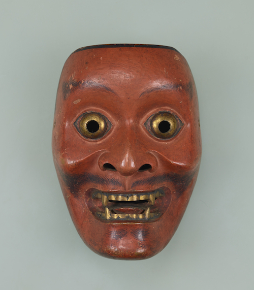 Nō-Maske mit Gesichtszügen eines Mannes, rot bemalt, aufgerissene Augen und Zähne golden bemalt