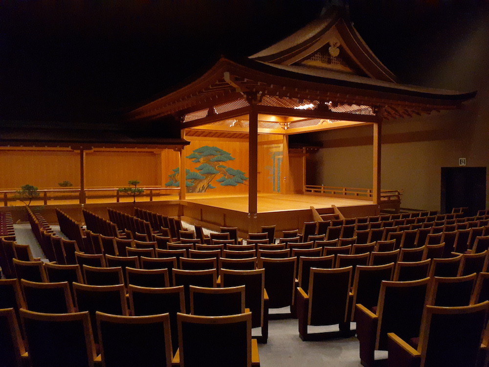 Nō-Bühne in einem Raum, im Vordergrund Sitzreihen für Zuschauer.