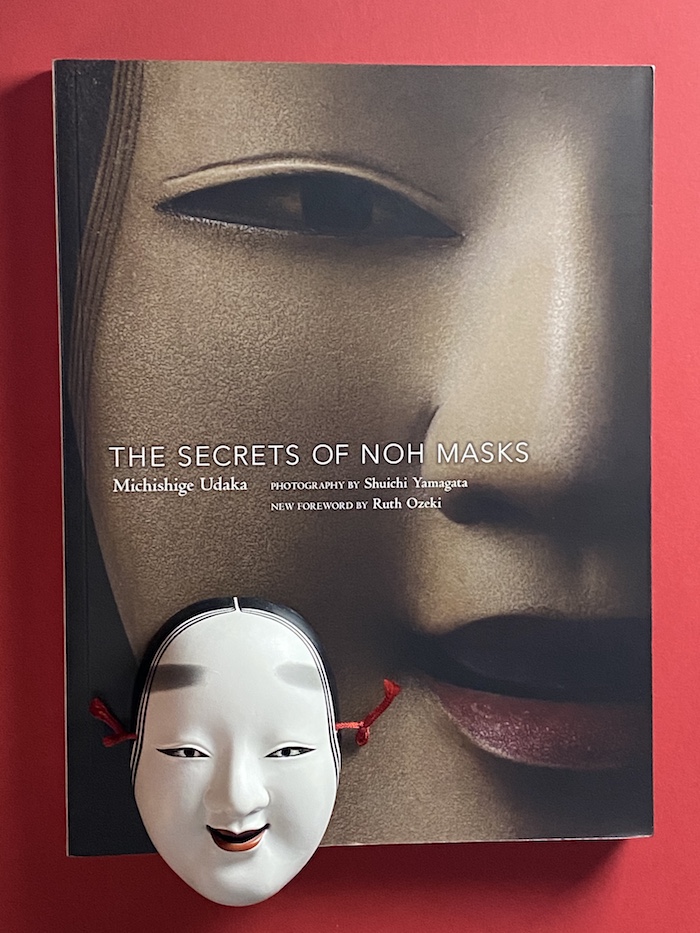 Buch „The Secrets of Noh Masks“, davor eine Nō-Maske für eine junge Frau (ko-omote) in Miniatur