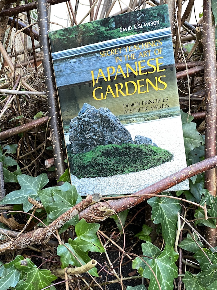 Das Buch "Japanese Gardens" vor Efeu und Ästen eines Haselnuss-Strauchs