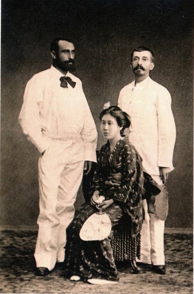 Zwei Herren in weißen Anzügen stehend, die Japanerin im Kimono in der Mitte sitzend. Alle Portraitierten schauen in verschiedene Richtungen.