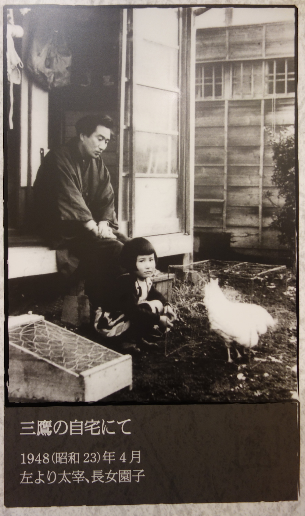 Vater und Tochter auf der Holzveranda eines Hauses, ein Huhn im Garten.