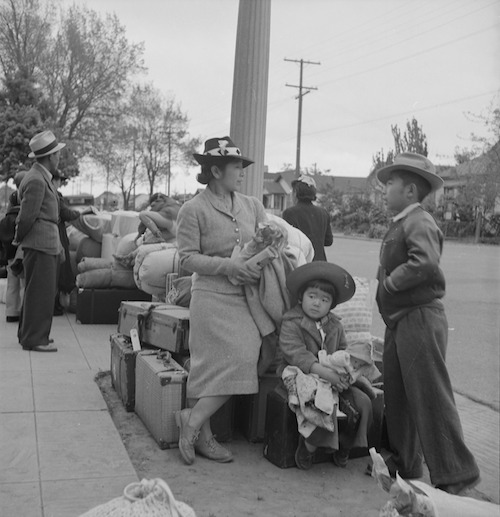 Gut gekleidete japanische Dame und zwei Kinder warten mit aufgestapelten Koffern und Kisten am Straßenrand.