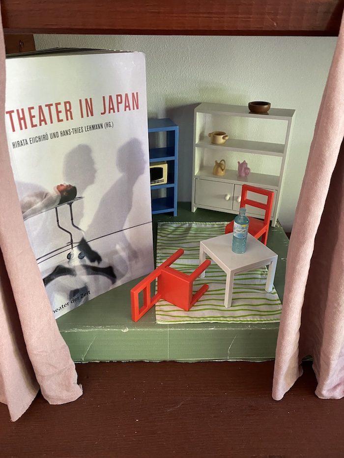Buch "Theater in Japan" auf einer Miniatur-Bühne mit einem Tisch, zwei Stühlen und Schränken