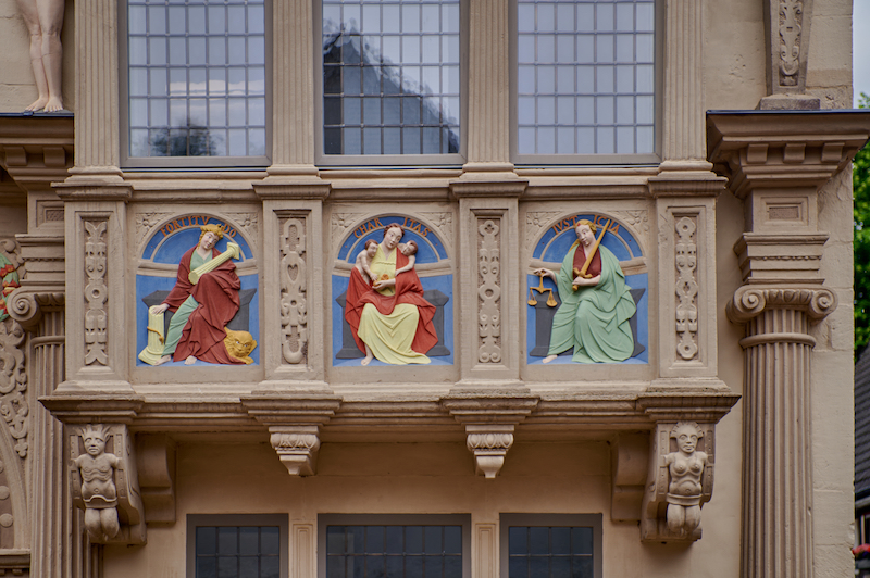 Ausschnitt aus der Fassade mit 3 bunten Frauenfiguren, die die Tugenden repräsentieren.