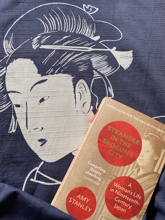 Buch vor einem dunkelblauen Stoff mit weißer Silhouette einer Frau aus der Edo-Zeit